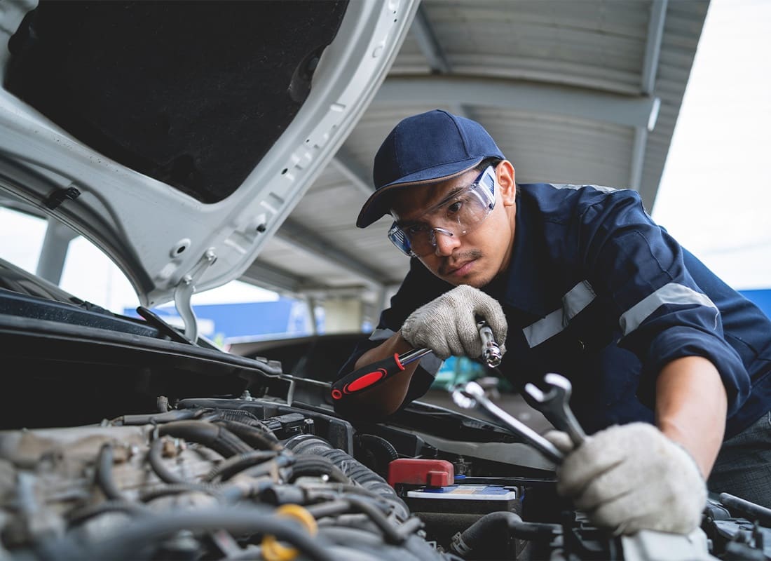 Insurance by Industry - A Male Mechanic Working on a Clients Car in a Repair Shop Whiling Wearing a Blue Cap
